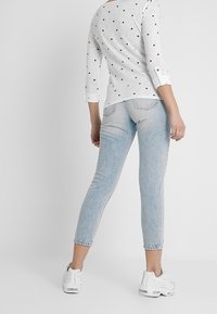 Ljust grå tröja med trekvartsärmar och små svarta stjärnmönster, kombinerad med ljusblå tajta jeans och vita sneakers.