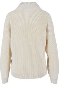 Béžový pletený svetr s vysokým límcem, žebrovanou strukturou, spadlými rameny a volným střihem. Má dlouhé rukávy a zaoblený spodní lem.