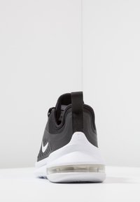 Nike tenisky s černým síťovaným svrškem, bílou podrážkou a viditelným vzduchovým polstrováním v patě. Mají strukturovaný vzor a poutko pro snadné obouvání.