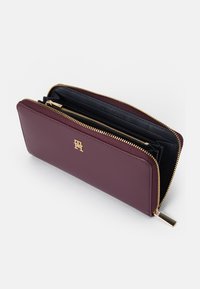 Portofel din piele burgundy cu accesorii aurii, închidere cu fermoar și interior negru. Dispune de mai multe sloturi pentru carduri și compartimente.