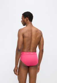 Κόκκινα βαμβακερά εσώρουχα με απαλό ύφασμα και ελαστική μέση με το λογότυπο "Calvin Klein". Απλός σχεδιασμός χωρίς σχέδια ή διακοσμήσεις.