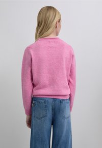 Bright pink knitted sweater with a ribbed crew neck and long sleeves, paired with light blue wide-leg denim jeans featuring back pockets.