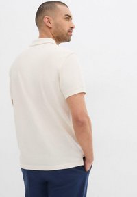 Polo shirt beige chiaro a maniche corte con colletto classico, morbido al tatto e orlo dritto, abbinato a pantaloni blu navy.
