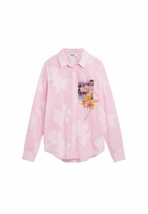 Rosa Hemd mit weißen Blumenmustern und einer Tasche, die eine Küstenstadt und eine große gelbe Blume zeigt.