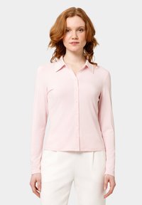 Camicia a maniche lunghe rosa con design abbotozzato, caratterizzata da un colletto e una texture liscia. La camicia è attillata, arrivando appena sopra la vita.