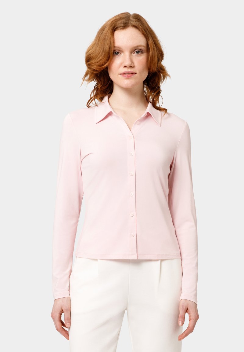 Camicia a maniche lunghe rosa con design abbotozzato, caratterizzata da un colletto e una texture liscia. La camicia è attillata, arrivando appena sopra la vita.