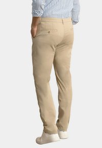 Chinos beige con corte ajustado, bolsillos traseros con botón y una textura de tela suave, combinados con zapatillas blancas.