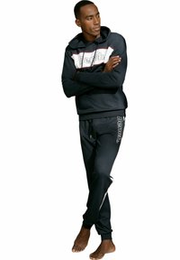 Schwarzer Hoodie mit roten und weißen Streifen, mit "Bench"-Logo. Kombiniert mit schwarzen Jogginghosen, die ebenfalls das "Bench"-Logo an der Seite zeigen.