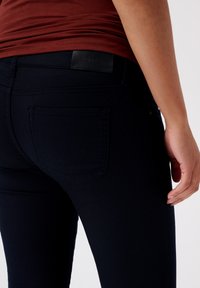 Mörk marinblå skinny jeans i denim, med en bakficka, läderlogotyppatch vid midjan och en slät, elastisk textur.