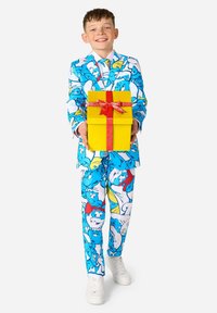 Kleurvol blauw en wit pak met cartoonfiguren, gecombineerd met een bijpassende stropdas en witte sneakers. Houdt een gele cadeau-doos vast met een rode strik.