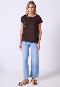 Top corto marrone a maniche corte con una vestibilità morbida, abbinato a jeans azzurri a gamba larga e sandali beige senza chiusura. Tessuto liscio e design semplice.
