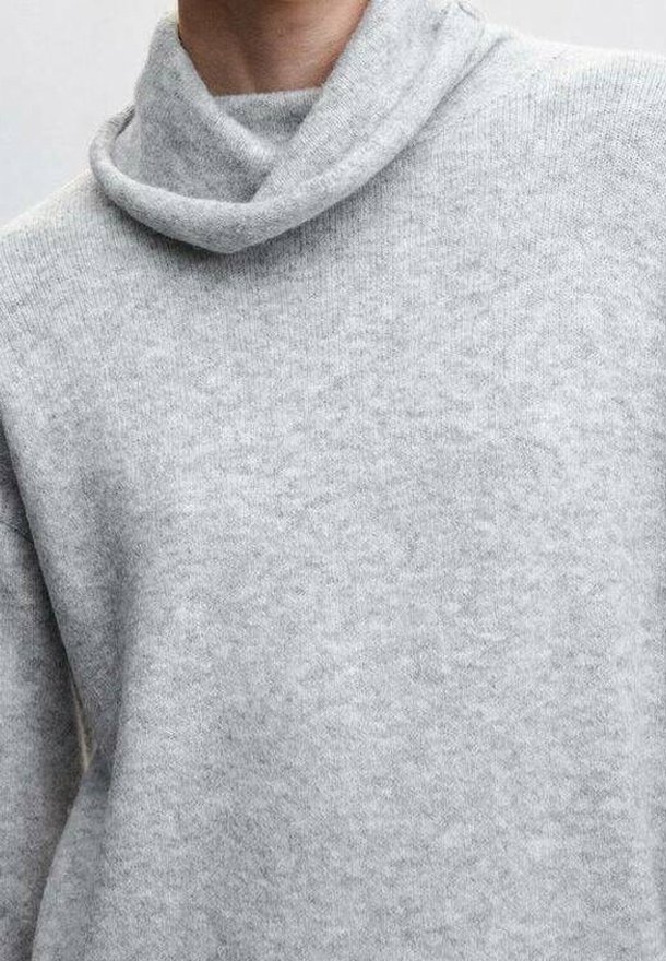 Personne portant un pull gris clair à texture douce avec un col roulé ample et replié.