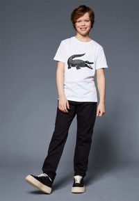 T-shirt blanche avec un graphique de crocodile noir, assortie à un pantalon noir et des baskets noires avec des semelles couleur crème. Design simple et décontracté.