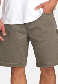 Șorturi cargo de culoare verde măsliniu, fabricate dintr-un material durabil, dotate cu buzunare laterale, o croială lejeră și detalii cusute pe șuvițe.