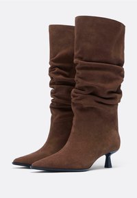 Bottines en daim marron au design décontracté, avec un bout pointu et un petit talon carré, présentant une texture lisse sans aucune pièce métallique visible.
