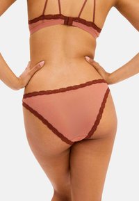 Ljusrosa underklädesset med delikat brunt spetskant, som har en bikinitrosa och en enkel design. Mjuk textur och sömlös finish.