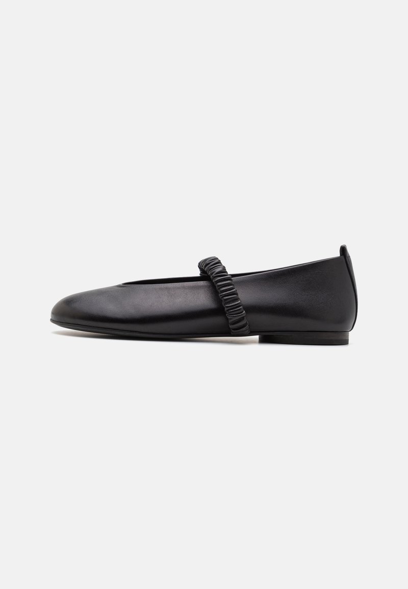 Chaussure plate en cuir noir avec une bride élastique froncée sur le dessus et un petit talon, vue de profil sur fond blanc.