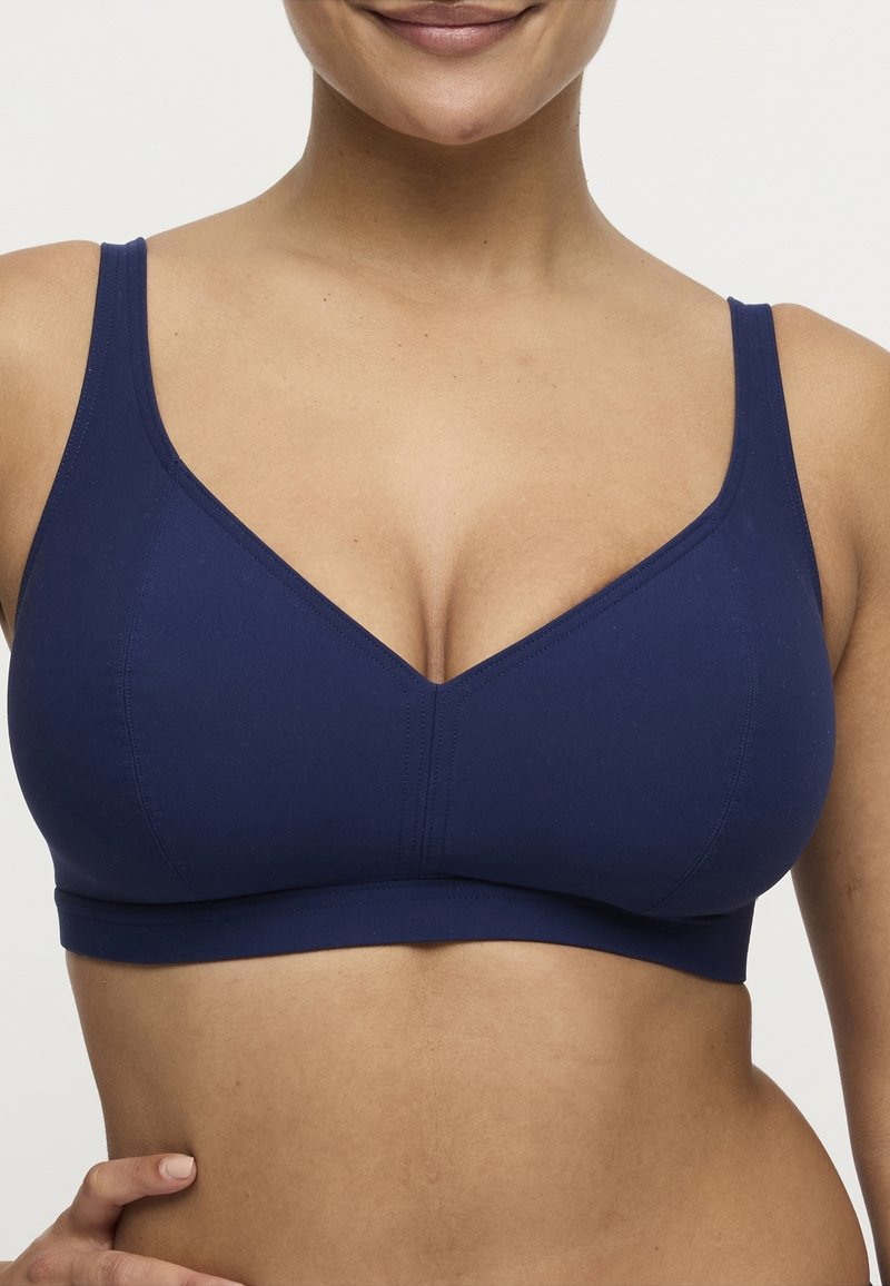 Marineblauwe beha met een naadloos ontwerp, brede bandjes en een V-vormige halslijn. Gladde textuur en medium ondersteuning, met een zachte band onder de buste.