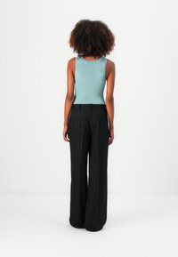 Un débardeur fin à rayures bleu clair associé à un pantalon taille haute à rayures noires, avec des poches avant et arrière.