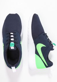 Tmavě modré tenisky z mesh materiálu se zelenými detaily a bílou podešví. Mají polstrovaný jazyk, zavazování na tkaničky a logo Nike na bocích i na jazyku.