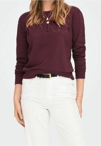 Felpa burgundy con "PARIS" in rilievo sulla parte anteriore, abbinata a jeans bianchi e una cintura nera, con una superficie liscia e polsini a coste.