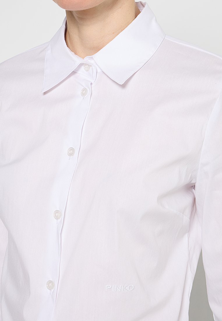 Helles pinke Hemd mit klassischem Kragen, transparenten Knöpfen und gesticktem Markenlogo am Saum. Glatter, strukturierter Stoff.