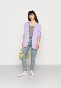 Blazer lilás, top cropped em xadrez preto e branco, jeans claros rasgados, ténis de cano alto lavanda e uma bolsa verde.