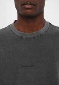 Mørkegrå sweatshirt med ribbet rund hals, der har et subtilt præglogo på forsiden. Materialet ser blødt og tekstureret ud.