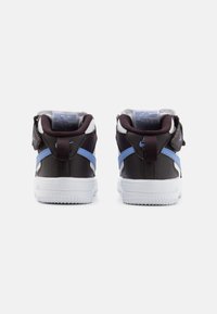 Sapatilhas Nike com parte superior castanho-escura, sola branca, realces azuis e colar almofadado, apresentando um design texturizado e detalhes de costura.