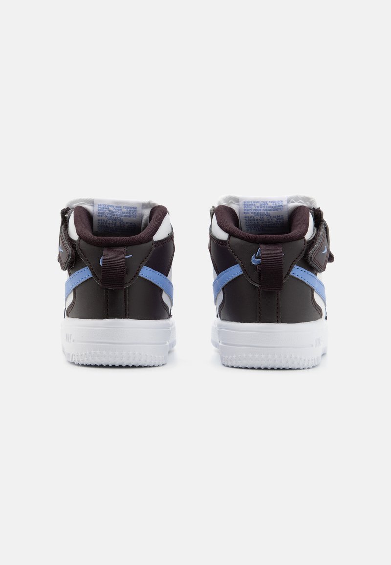 Baskets Nike avec un upper marron foncé, une semelle blanche, des accents bleus et un col rembourré, comprenant un design texturé et des détails de couture.