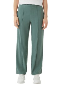Light green, wide-leg pants made of a smooth fabric. Features front pleats and a high waist. Paired with white sneakers.