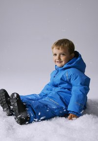 Blue winter snowsuit with a hood, featuring elastic cuffs, side pockets, and a smooth texture, worn by a child sitting in snow.