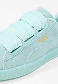 Baskets Puma Suede bleu clair avec larges bandes en tissu et semelle en caoutchouc, montrant une texture détaillée en daim et un logo Puma doré.