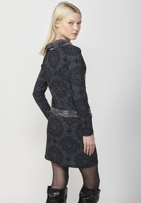 Langarmkleid aus strukturiertem schwarzem Stoff mit einem gemusterten Design. Verfügt über einen einzigartigen Kragen und einen reflektierenden silbernen Gürtel in der Taille.
