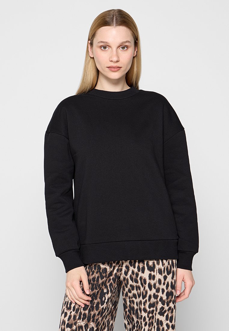 Zwarte sweatshirt met een ronde hals, drop shoulders en geribde manchetten. Gedragen met een pantalon met een patroon van luipaardprint. Gladde textuur.