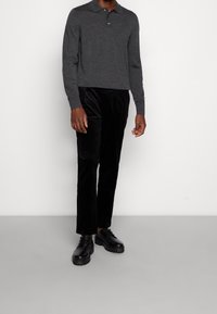 Mörkgrå polotröja med långa ärmar och krage, kombinerad med svarta sammetsbyxor och svarta snörskor med grova sulor.