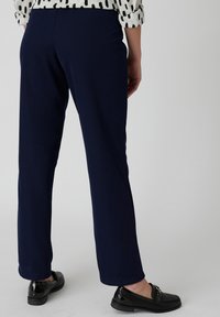 Navyblauwe broek met een rechte snit, gemaakt van een gladde stof, met een subtiele textuur en een schone tailleband. Gecombineerd met glanzende zwarte instappers.