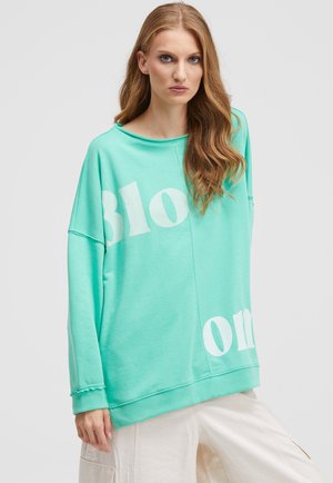 Mintgrünes, übergroßes Sweatshirt mit "Bloom" in Weiß bedruckt. Hat einen weiten Ausschnitt und strukturierte Bündchen. Aus weichem, lässigem Material.