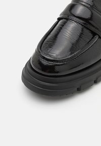 Zwarte gepatineerde leren loafers met een ronde neus, voorzien van een dikke zwarte rubberen zool en slanke horizontale bandaccenten.