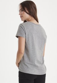 Grå kortærmet t-shirt med rund halsudskæring og let buet kant, lavet af blødt stof og med en afslappet pasform. Bæret med sorte bukser.