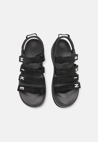 Sandales noires avec quatre straps Velcro ajustables arborant le logo "NIKE" en blanc. La semelle est texturée pour une meilleure adhérence et un confort optimal.