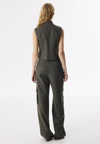 Gilet sans manches ajusté vert et pantalon cargo large assorti avec poches latérales, fabriqué en tissu texturé, vu de dos.