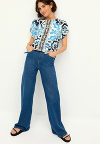 Blommönstrad kortärmad topp i blått, vitt och svart, tillsammans med högmidjade, löst sittande mörkblå jeans. Enkla svarta sandaler.