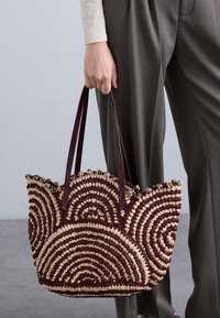 Πλεκτή τσάντα ώμου με σπειροειδές σχέδιο σε καφέ και μπεζ χρώμα, φτιαγμένη από υφαντή λόγχη και με σκούρες καφέ δερμάτινες ιμάντες.