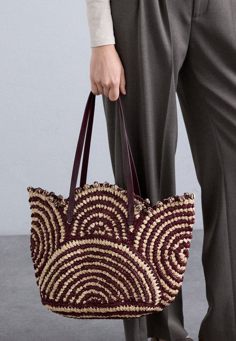 Πλεκτή τσάντα ώμου με σπειροειδές σχέδιο σε καφέ και μπεζ χρώμα, φτιαγμένη από υφαντή λόγχη και με σκούρες καφέ δερμάτινες ιμάντες.