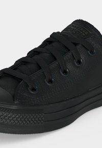Μαύρο χαμηλό sneaker από δέρμα με υφή στη λαστιχένια σόλα και μαύρα κορδόνια που περνούν από έξι οπές σε λευκό φόντο.