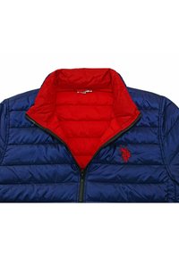 Tmavě modrá péřová bunda s červenou vnitřní podšívkou, vybavená zipem vpředu, prošívanou texturou a vyšitým logem na levé straně hrudi.