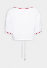 Top blanc court avec un large décolleté, de courtes manches bouffantes, une bordure rouge le long du décolleté et des bords des manches, et un détail de lien dans le dos.