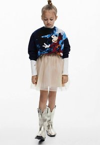 Pusa, millel on tumedal taustal värvikas graafika, kihiliselt üleval õhukese tulelise seeliku, kombineeritud metalliliste hõbedaste cowboy-saapadega.