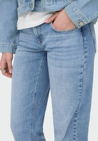 Svijetloplavi traperice ravnog kroja, s blagim izblijedjelim dijelovima, klasičnim džepovima i uskim strukom. U kombinaciji s ležernim sakoom.